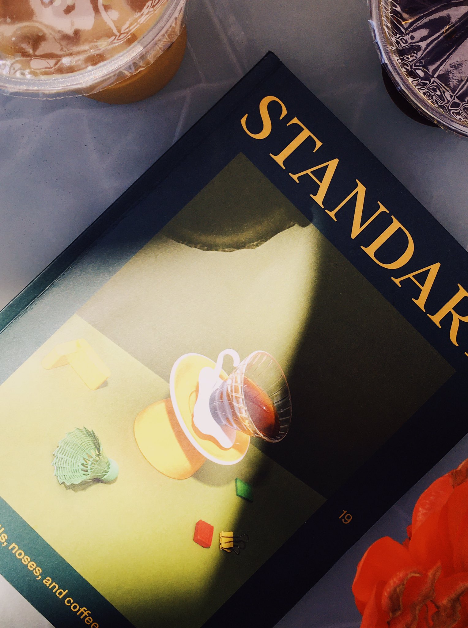 A dramatic sunbeam over a magazine, next to some iced drinks and red flower petals.